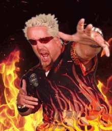 a gif of Guy Fieri wearing his classic fire print button down and posting bombastically. There is an exaggerated heat distortion applied to the photo. The background is a stock photo of fire being wiggled around erratically.