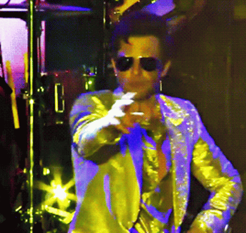 #PRATODOSVEREM: um cantor, num show, veste um terno dourado e olha para a frente do palco, apontando para diversas direções. 